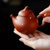 Close-up of a Yixing Clay Gongfu Tea Set teapot held gently in hands, showcasing the premium red clay texture and gold speckle details against a black background