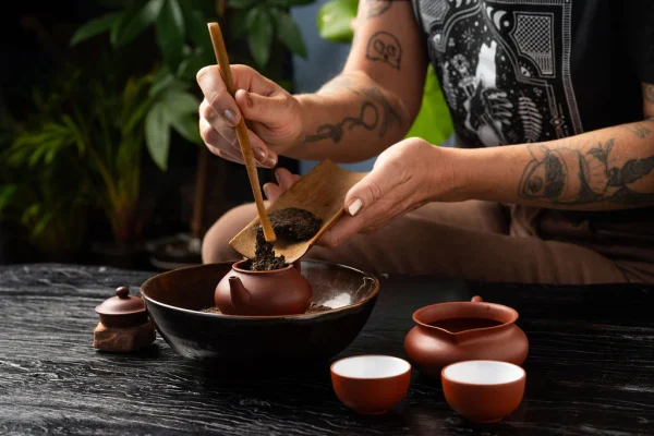 using a tea scoop to add tea leaves into the Yixing clay teapot from a bamboo tea tray