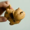 Angled view of a Yixing Cat tea pet, a charming golden clay cat tea pet with hand-painted details, held in a hand to showcase its three-dimensional shape and playful expression