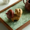 Yixing Cat tea pet serving as a teapot lid rest, a handmade golden clay cat tea pet with colorful floral patterns, displayed on a fabric-covered gongfu tea tray with a Yixing teapot in the background