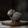 Grey clay Yixing Sheep Tea Pet with a detailed, coin-patterned wool coat, displayed on a wooden disc for elegant tea table decor