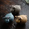 Set of three Yixing Sheep Tea Pets in grey, blue, and golden clay, arranged on a dark wooden surface to highlight their unique color variations