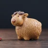 Golden clay Yixing Sheep Tea Pet with a playful expression, presented on a dark wooden surface with a dried flower for a cozy tea room aesthetic