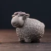 Grey clay Tea Pet Yixing shaped as a sheep, featuring a coin-patterned wool coat, displayed on a dark wooden base for a minimalist tea setup