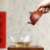 Pouring tea from a Yixing Lotus Purple Clay Teapot into a glass pitcher, showcasing the functional design of this Yixing Lotus Pottery teapot for gongfu tea ceremonies