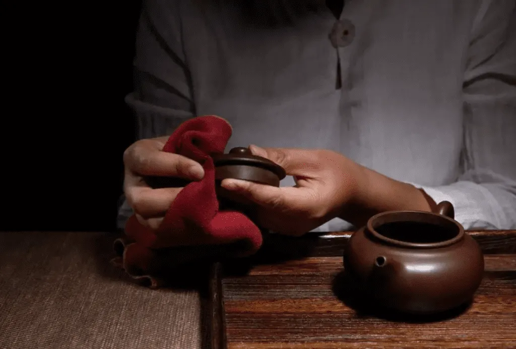 How to Clean and Maintain an Yixing Teapot 1 How to Clean Yixing Teapot: A person gently wiping the lid of a Yixing teapot with a soft cloth, demonstrating proper Yixing teapot care.