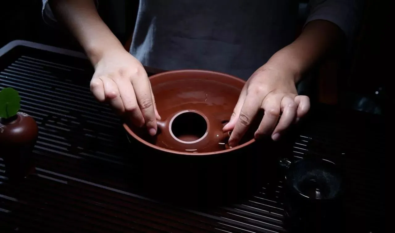 How to Clean and Maintain an Yixing Teapot 2 How to Clean Yixing Teapot: Hands rinsing a Yixing teapot in clean water, a key step in Yixing teapot care to remove tea residue.