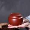 Hands holding a round Yixing Tea Caddy, highlighting its compact size, glossy finish and ergonomic design for daily tea use