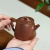 Crafted Yixing Purple Clay Teapot from Yixing Zisha Tea Set, held in hand to showcase its elegant design, a premium piece in Yixing Tea Sets