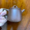 Elegant Yixing Purple Clay Teapot from Yixing Zisha Tea Set, held to display its traditional shape, a key component of Yixing Clay Tea Set