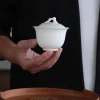 Hand holding a 100 ml white porcelain gaiwan, showcasing its elegant shape against a dark background