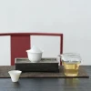 100 ml white porcelain gaiwan on a dark tea tray, with a glass pitcher of tea and a teacup, set against a red chair