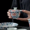 Holding an Antique Gaiwan adorned with vibrant goldfish artwork, highlighting the craftsmanship of this Best Gaiwan Tea Set.