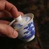 Holding the lid of a 60ml Gaiwan, a Small Gaiwan with blue and white landscape patterns, demonstrating its easy handling.