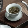 Celadon Gaiwan teacup filled with loose tea leaves, placed on a wooden tea tray, ready for the gongfu tea brewing ritual.
