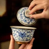 Lifting the lid of a Chinese Gaiwan Tea Set, showcasing intricate blue and white floral patterns on this porcelain gaiwan.