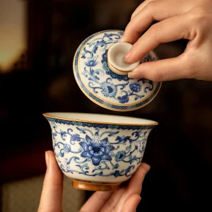 Lifting the lid of a Chinese Gaiwan Tea Set, showcasing intricate blue and white floral patterns on this porcelain gaiwan.