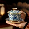 Holding a complete Porcelain Gaiwan Tea Set, featuring a gaiwan, lid, and saucer with traditional blue and white floral motifs.