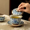 Uncovering a Chinese Gaiwan Tea Set filled with golden tea, revealing the smooth interior and delicate blue and white exterior.