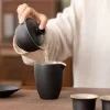 Pouring tea from a Black Gaiwan into a matching fairness pitcher, showcasing the smooth pouring design of this matte black ceramic tea set.