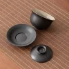 Disassembled Black Gaiwan set, featuring the bowl, lid, and saucer, highlighting the textured black ceramic and contrasting light interior.