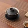 Black Gaiwan with lid resting on a bamboo tea mat, paired with a teacup of brewed tea for a minimalist, modern tea time setup.