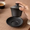 Holding the bowl of a Black Gaiwan above its saucer, demonstrating the separate components of this classic three-piece tea set.