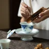 Adding tea leaves to a Dehua Gaiwan on a raised saucer, capturing the traditional tea preparation process.