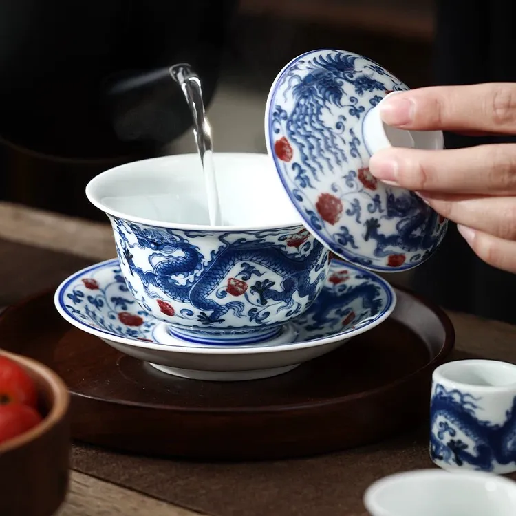 Dragon and Phoenix Auspicious Stoneware Gaiwan 165ml 3 Lifting the lid of a Stoneware Gaiwan to pour water, showcasing intricate blue and white dragon motifs on this Dragon Gaiwan.