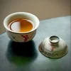 Gaiwan Pot filled with amber tea, with its lid placed beside to showcase the smooth, hand-painted butterfly and floral design during a tea ceremony.