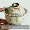 Holding a full-bodied Gaiwan Pot, showcasing its hand-painted butterfly and floral motifs and classic, elegant shape for refined tea preparation.