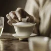 Lifting the lid of a Gaiwan Porcelain to reveal steeping tea, capturing the quiet ritual of traditional tea preparation.
