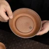 Holding an Unglazed Gaiwan tea tray, highlighting its concentric ridged patterns and handcrafted artisan seal