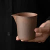 Unglazed ceramic pitcher from the Gaiwan tea set, held to display its earthy, matte finish and functional spout