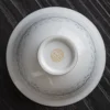 Close-up of the base of a Porcelain Gaiwan, featuring a golden brand mark and subtle rice pattern details on the translucent porcelain.