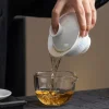 Pouring tea from a Rice Pattern Gaiwan into a glass pitcher, demonstrating the smooth pouring function of this premium porcelain gaiwan.