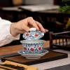 Hand lifting the lid of a Glazed Porcelain Gaiwan, demonstrating the gongfu tea brewing process.