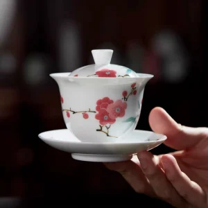 Hand holding a complete Mei Leaf Gaiwan with delicate red blossom and bamboo patterns, showcasing its elegant white porcelain body