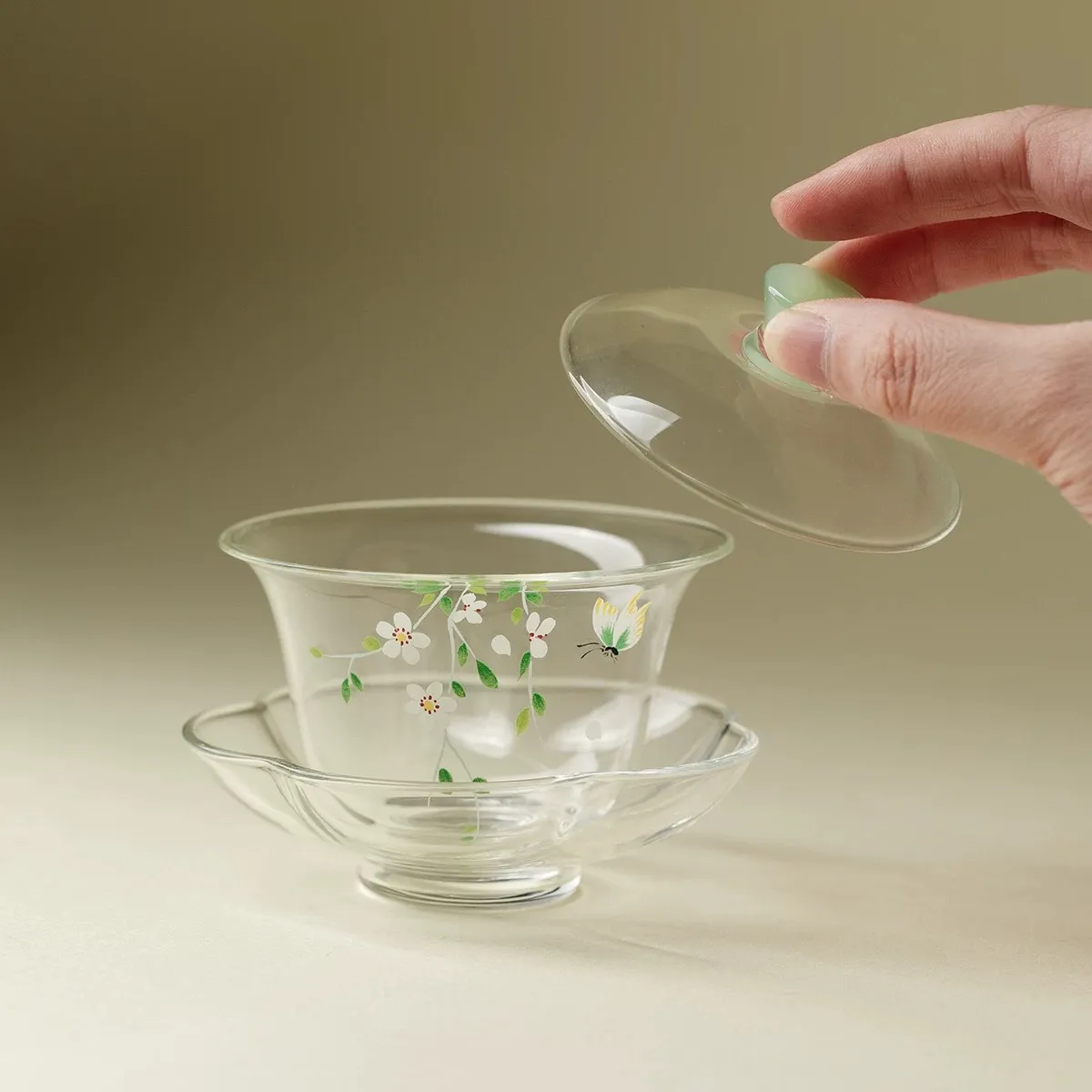 Made of Borosilicate Glass Gaiwan 95ml 3 Gaiwan Made of Borosilicate Glass with lid lifted, revealing hand-painted floral and butterfly artwork inside, resting on a matching flower-shaped glass saucer.