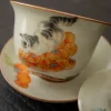 Close-up of a Cat Gaiwan, showcasing hand-painted cat and persimmon artwork on crackled ceramic, highlighting delicate craftsmanship.