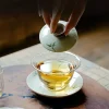 Uncovering the lid of a Gaiwan Glass, revealing the brewed tea inside, with delicate bamboo designs on the lid.