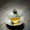 Gaiwan Glass filled with golden tea, placed on a wooden table, with subtle bamboo patterns enhancing its aesthetic appeal.