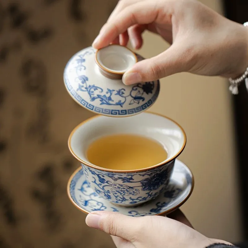 Traditional Blue and White Ru Kiln Gaiwan Tea Set 140 ml 3 Lifting the lid of a Ruyao Gaiwan to reveal amber tea inside, demonstrating the elegant use of this Traditional Gaiwan Tea Set for daily tea enjoyment.
