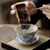 Traditional Blue and White Ru Kiln Gaiwan Tea Set 140 ml 11 Adding tea leaves to a Ruyao Gaiwan, capturing the traditional tea preparation process with this exquisite Traditional Gaiwan Tea Set.