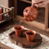 Pouring tea from a Yixing Pumpkin Purple Sand Teapot into two matching teacups, showcasing the elegant pouring action.
