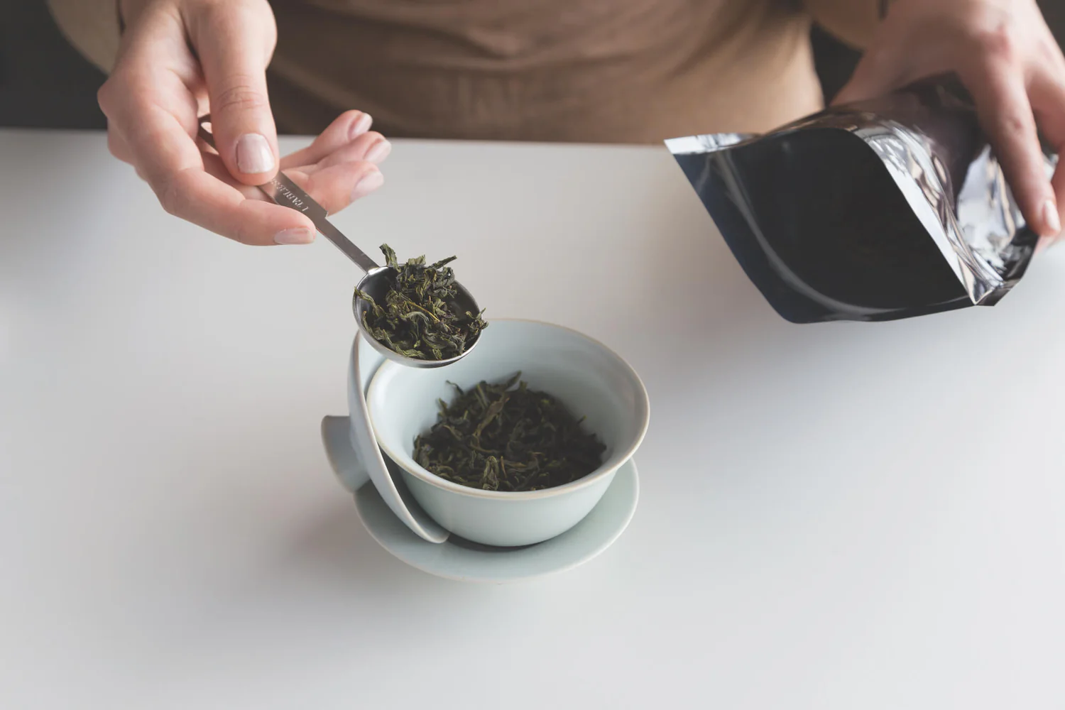 Step 2 of how to use a gaiwan: adding measured loose leaf tea into a porcelain gaiwan with a tea spoon